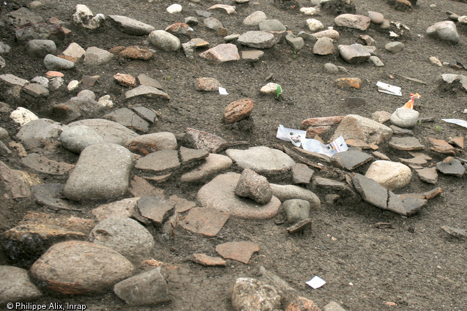 Vue rapprochée d'un niveau de sol du Néolithique moyen chasséen (IVe millénaire avant notre ère) sur le site des Queyriaux à Cournon-d'Auvergne (Puy-de-Dôme), 2011.  Des galets et le mobilier - ici de gros fragments de céramique - posés à plat jonchent le sol.