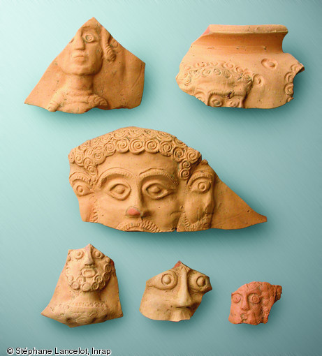 Fragments de vases à bustes montrant des divinités, IIIe s. de notre ère, Famars (Nord), 2008.  Au centre Mercure et son visage tricéphale. Pour ce type de vase, le nombre de bustes est basé sur le principe des jours de la semaine, un concept surtout connu dans le culte du dieu Mithra où les 7 jours de la semaine et les 7 niveaux de l'initiation au culte sont fondamentaux. Typiques de la cité des Nerviens, ces vases portent 6 ou 7 bustes représentant des divinités. 