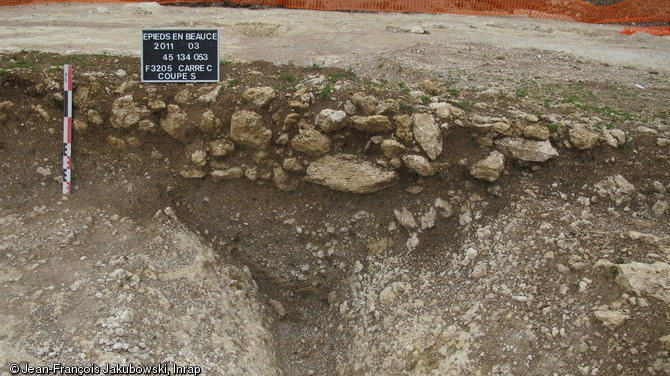 Coupe du fossé d'enclos avec scellement de pierres calcaires, Ier s. de notre ère, Épieds-en-Beauce (Loiret), 2011.  Le site, fossés compris, était scellé uniformément par des pierres calcaires locales qui ont permis une conservation exceptionnelle de la stratigraphie sur 70 cm d'épaisseur. 