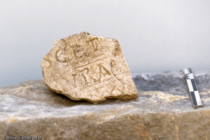 Fragment de plaque funéraire avec inscription, Metz (Moselle), 2012.  La diversité des modes d'inhumation et du mobilier funéraire atteste une utilisation du cimetière durant plusieurs siècles au Moyen Âge. 