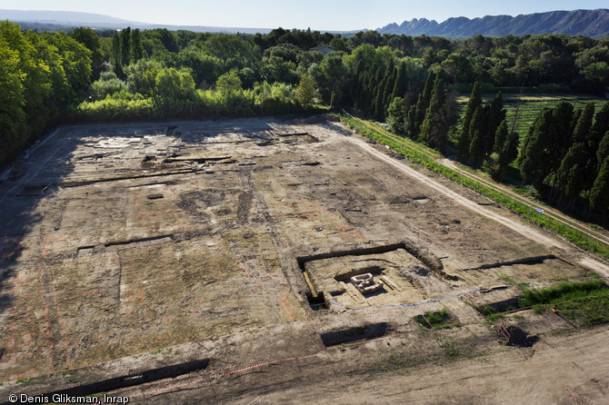 Le mausolée au milieu des parcelles cultivées avec en arrière-plan la villa, IIe-Ve s. de notre ère, Saint-Rémy-de-Provence (Bouches-du-Rhône), 2012.Les vestiges dégagés appartiennent à la partie résidentielle de la villa. Les différents bâtiments sont édifiés au IIe s., transformés au IIIe et abandonnés au Ve s.