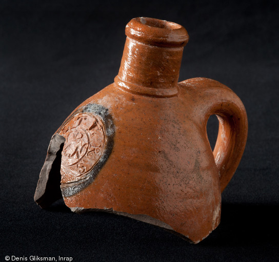 Bouteille incomplète en grès produite dans le Westerwald (Rhénanie-Palatinat) au XVIIIe ou XIXe s. mise au jour place du Château à Strasbourg (Bas-Rhin), 2012.  Elle porte un cachet composé d'un cercle bleu dans lequel sont inscrites les lettres  SELTERS , le dessin d'une couronne ainsi que les lettres  HN , H(erzogthum) N(assau). 