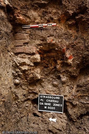 Vue d'un mur observé en suivi de réseau dans une tranchée creusée place du Château à Strasbourg (Bas-Rhin), 2012.  La structure est un angle de bâtiment dont la base de la maçonnerie est constituée de tuiles romaines plates à rebord (tegula) superposées les unes sur les autres. 