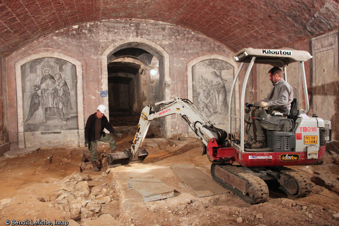 Décapage mécanisé dans la crypte de la basilique Notre-Dame de Boulogne-sur-Mer (Pas-de-Calais), 2012. Dans la nef de la crypte, la fouille a mis en évidence des niveaux archéologiques antérieurs à la construction des premiers remparts connus du camp de la classis britannica, datés du début du IIe s. L'espace se structure selon un  quadrillage  urbain très régulier dès le milieu ou la seconde moitié du Ier s. de notre ère.                           <br