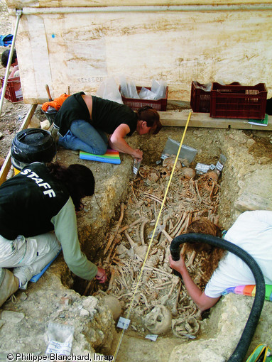 Nettoyage d'une sépulture multiple de la fin du XVIIe ou du début du XVIIIe s. après prélèvements des individus du premier niveau, Issoudun (Indre), 2002.   Photo publiée dans le numéro 19 de la revue de l'Inrap Archéopages. 