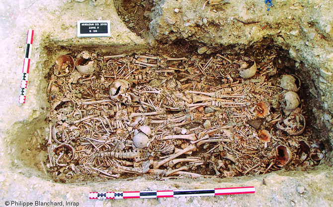 Vue verticale d'une sépulture multiple datée de la fin du XVIIe ou du début du XVIIIe s. et mise au jour à Issoudun (Indre) en 2002.Les défunts correspondent majoritairement à des immatures (moins de 18 ans) très certainement décédés lors d'une crise épidémique, peut-être la variole suite au grand hiver de 1709 ?   Photo publiée dans le numéro 19 de la revue de l'Inrap <a class= rte-link-ext  href= http://www.inrap.fr/archeologie-preventive/Recherche-scientifique/Archeopages/Les-numeros/18-19-20-2007/Numero-19/Pratiques/p-9414-Strategie-de-fouille-d