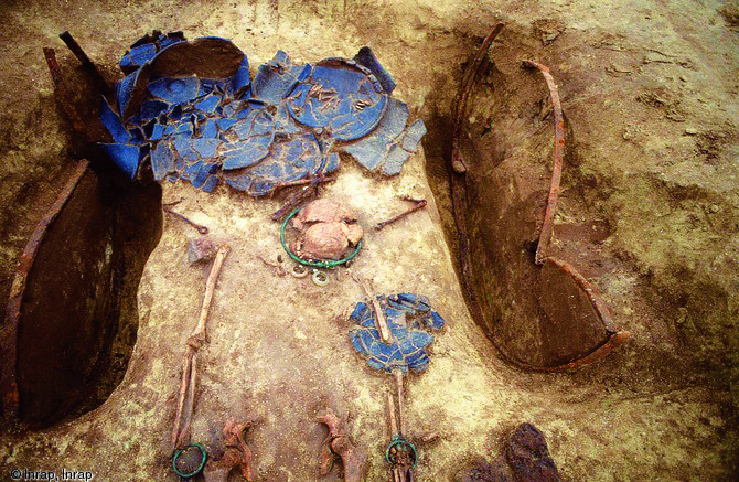 Tombe à char, Ve-IVe s. avant notre ère, Bucy-le-Long (Aisne), 1994.La tombe présente un aménagement du fond constitué de deux fosses servant à accueillir les roues du char dont ne subsistent plus que les cerclages. La défunte, déposée à plat sur le char, porte un torque torsadé en bronze à incrustation de corail. A l'arrière du char on trouve de la vaisselle contenant une partie des offrandes alimentaires.    Photo publiée dans le numéro 19 de la revue de l'Inrap <a class= rte-link-ext  href= http://www.inrap.fr/archeologie-preventive/