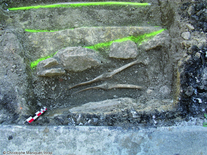 Sépulture constituée de pierres posées de chant le long des parois du creusement et datée entre les XIIe et XIVe s., Saint-Junien (Haute-Vienne), 2009.Ici seules les jambes du défunt ont été dégagées.
