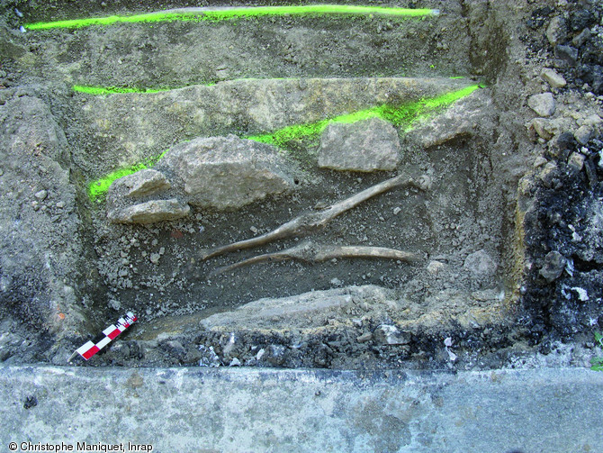 Sépulture constituée de pierres posées de chant le long des parois du creusement et datée entre les XIIe et XIVe s., Saint-Junien (Haute-Vienne), 2009.Ici seules les jambes du défunt ont été dégagées.