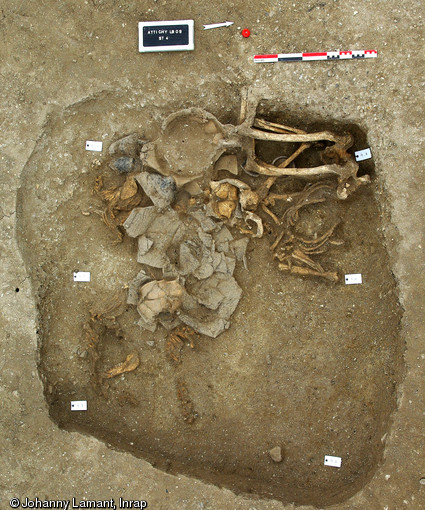 Vue générale de la sépulture d'un homme plié , IIIe s. avant notre ère, Attichy (Oise), 2009.L’homme d’âge adulte est déposé sur le dos en position fœtale, le regard orienté vers le septentrion, le corps décalé de 90° par rapport à la pratique « admise » au sein de cette nécropole. Malgré cette singularité, on note un rituel similaire aux autres sépultures avec la présence de très nombreuses offrandes alimentaires.