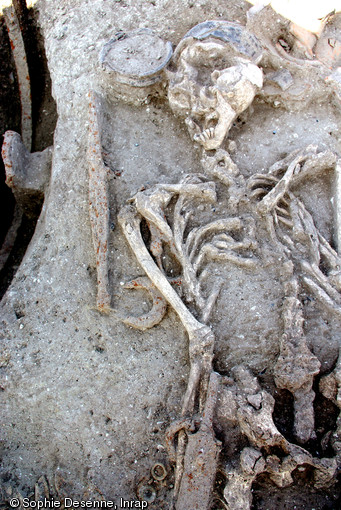 Vue de détail d'une tombe à char de la nécropole d'Attichy (Oise), IIIe s. avant notre ère, 2009. On distingue une pointe de lance et, au premier plan, une épée accompagnée d'anneaux en bronze, dernières traces de son système de suspension et du ceinturon.