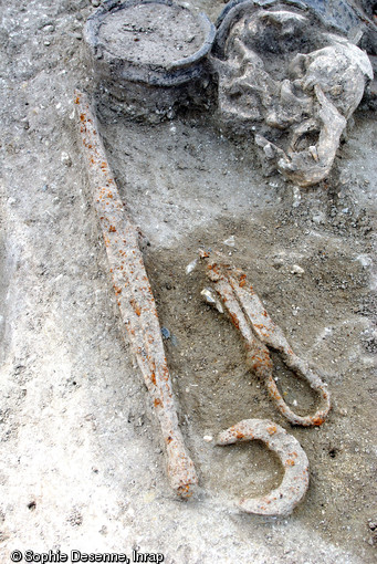 Vue de détail du mobilier métallique accompagnant un défunt inhumé dans une tombe à char à Attichy (Oise), IIIe s. avant notre ère, 2009.   Il se compose d'armes (épée et lance, dont la pointe apparaît ici), d'un rasoir et d'une paire de force qui évoquent la toilette ou une activité artisanale (travail de la laine ou des peaux).