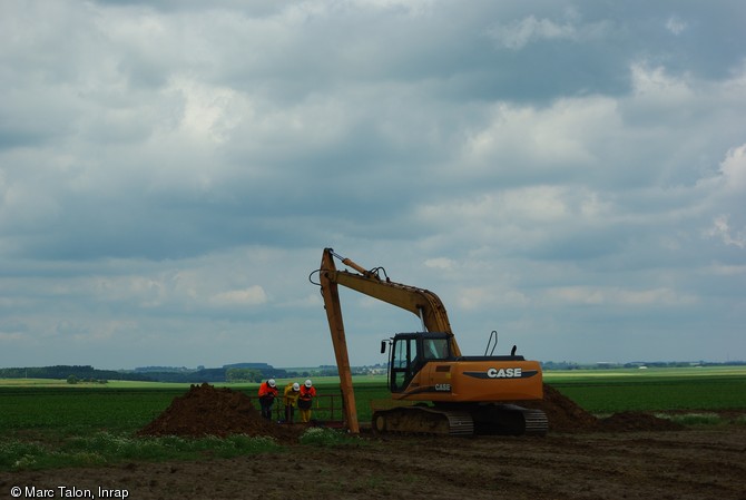 Campagne de sondages profonds avec utilisation d'une pelle hydraulique à bras rallongé sur le tracé du Canal Seine-Nord Europe dans le Pas-de-Calais en 2009.  Le balcon-passerelle permet aux archéologues de se pencher sans danger pour observer et relever la stratigraphie. Ce type de pelle permet de réaliser des sondages en puits jusqu'à 14 m de profondeur.