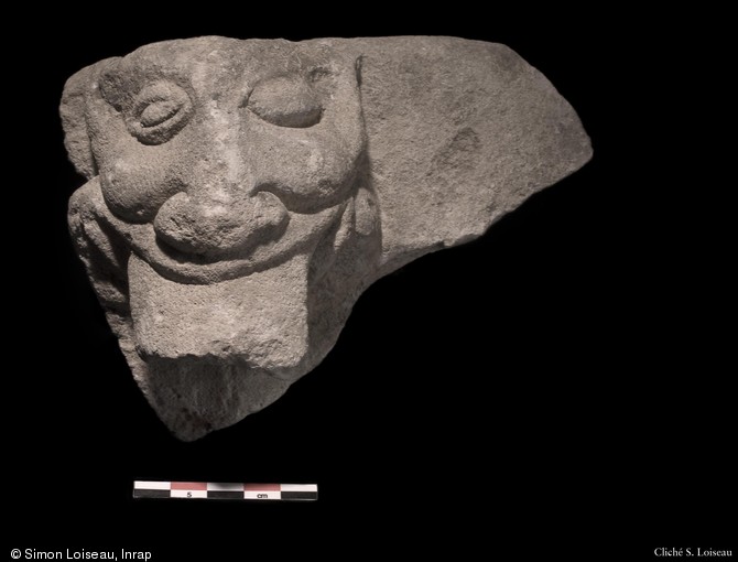 Fragment du rebord d'une cuve d'un récipient en pierre décoré d'une figure anthropomorphe, peut être daté du XIIIe s. et retrouvé en réemploi dans une halle commerçante du XIVe s., Lagny-sur-Marne (Seine-et-Marne), 2010.