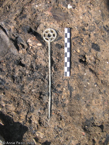 Épingle en bronze à extrémité décorée d'une rouelle, Xe-IXe s. avant notre ère, Amélie-les-Bains (Pyrénées-Orientales), 2006.Cet élément de parure a été perdu ou abandonné sur le sol d'une cabane, aux côtés de vases fragmentés et d'ossements consommés.  