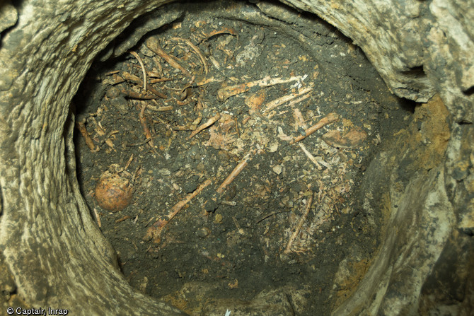Vue générale d'un niveau de sépulture présentant, en haut légèrement à gauche, un individu en connexion partielle assis contre la paroi, VIIIe-Xe s., Entrains-sur-Noahain (Nièvre), 2013. Dans un puits antique de l'agglomération d'Intaranum, 20 à 30 corps ont été jetés simultanément, victimes d'un massacre ou d'une épidémie à dater entre les VIIIe et Xe s.