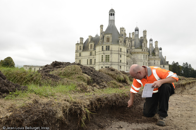 Fouille des vestiges visibles dans la coupe réalisée dans la partie orientale du site, château de Chambord (Loir-et-Cher), 2013.Les traces laissées par les jardins sont éphémères et difficiles à lire en surface dans le contexte d'un substrat composé de remblais hétérogènes. Leur identification nécessite l'observation fine des changements de sédiments. En arrière-plan, la tour de l'angle nord-est de l'enceinte du château.