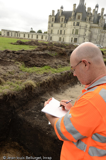 Enregistrement d'une des fosses de plantation du bosquet de marronniers qui occupait le carré nord-est du jardin anglais, château de Chambord (Loir-et-Cher), 2013.Les trous de plantation apparaissent comme des tâches sombres de 2,60 à 3 m de diamètre en surface. La fouille partielle permet d'observer la forme de la fosse d'origine et de son comblement, en partie effacés par le dessouchage de l'arbre.