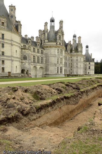 L’extrémité orientale du sondage est-ouest, implanté parallèlement à la façade nord du château, Chambord (Loir-et-Cher), 2013.La coupe stratigraphique permet de voir les fosses de plantation et des vestiges des allées sablées du jardin « à la française » du XVIIIe siècle, concentrés dans une couche de remblais épaisse de 30 à 40 cm située immédiatement sous la terre végétale actuelle. Sous cet horizon, on observe des niveaux de sables stériles apportés soit par l’action du Cosson soit en remblai pour combler le fond de la vallée et rehausser le terrain de presque 3 mètres avant