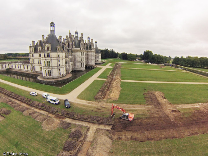 Vue générale du site prise depuis l’est en regardant vers l’ouest, Chambord (Loir-et-Cher), 2013.Le château et les parterres forment un espace carré de 280 m de côté, divisé en quatre quarts. Le château occupe le quart sud-ouest tandis que les parterres s’étendent sur les trois autres quartiers en forme de « L ». Le cliché montre les deux sondages principaux, implantés nord-sud et est-ouest afin de donner une vision de la stratigraphie dans les axes principaux.