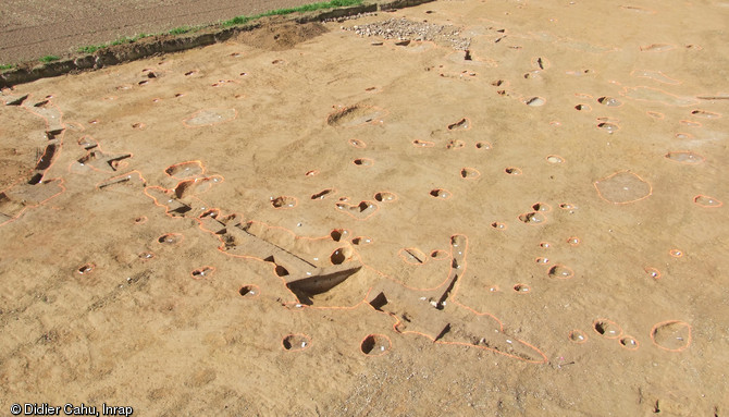 Vue d'un secteur de la fouille menée à Vassé, Torcé (Ille-et-Vilaine), 2012. Au premier plan, on observe un fossé moderne, puis une concentration de structures des VIIe-IXe s. (trous de poteaux, silos enterrés, structures de combustion). Au fond, la zone empierrée est un chemin moderne lié au manoir voisin construit au XVIe s.