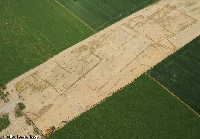 Vue aérienne du site après décapage, VIIe-Xe s., Vassé, Torcé (Ille-et-Vilaine), 2012.Les nuances d'humidité révèlent le parcellaire. Délimitées par des fossés, les parcelles ont connu divers aménagements au cours du temps : habitat, exploitation agricole...