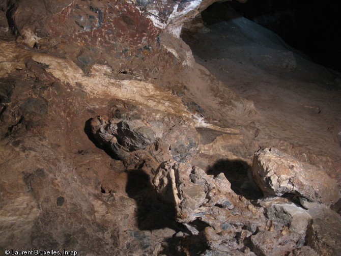 Afin de connaître l’âge du fossile, il importe tout d’abord de bien comprendre la stratigraphie du site, c'est-à-dire la relation entre les couches de sédiments et le squelette de Little Foot.On distingue ici les niveaux de brèches (de couleur foncée) et les  concrétions de calcite blanche lentement déposées  par les eaux d’infiltration.