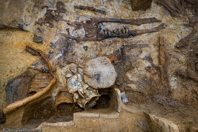 Squelette d'un aristocrate gaulois sur son char daté du IIe siècle avant notre ère, mis au jour à Warcq (Ardennes), en 2014.  Le défunt est entouré d'un mobilier composé d'un bandage de roue, d'un fragment de bois semi-circulaire recouvert de feuille d’or, d'objets en bronze liés à la caisse du char, du crâne d’un des chevaux et d'un disque en bois recouvert de feuilles d’or placé sur plusieurs céramiques.