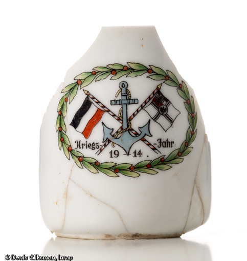 Tasse en porcelaine à motif patriotique. Blason constitué d'une couronne de laurier, d'une ancre de marine, du drapeau national allemand à gauche et celui de l'armée impériale à droite. Inscription  Kriegs Jahr 1914  (Année de guerre 1914). Pas de marque de fabricant. Découverte dans une latrine d'un terrain d'aviation allemand datant de la Grande Guerre à Warmeriville (Marne), 2013.