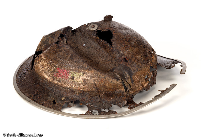 Casque d'acier britannique modèle  Mark II  de Beach Groups en dotation au cours de la Seconde Guerre mondiale. Sa forme particulière le fait surnommer le  plat à barbe  et malgré son état, il conserve encore un profil reconnaissable ainsi que des bandes de peinture d'identification encore visibles (d.30cm). Découvert à Saint-Aubin-d'Arquenay (Calvados), 2013.