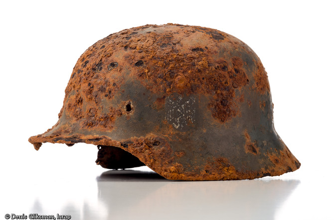 Casque allemand en acier (stahlhelm), modèle 1935 (d. 25 cm et h. 25 cm), marqué d'un écusson avec une croix gammée. Ce casque a reçu une peinture anti-reflet, probablement appliquée par le soldat sur le terrain. Datant de la Bataille de Normandie (été 1944) et découvert à Troarn (Calvados), 2009.