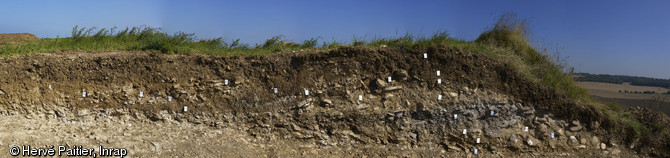 Coupe stratigraphique sur le site du Mont Castel à Port-en-Bessin (Calvados), 2014.  De bas en haut : couche noire, âge du Bronze final ; couche blanche, La Tène ancienne ; couche brune, rempart romain. 