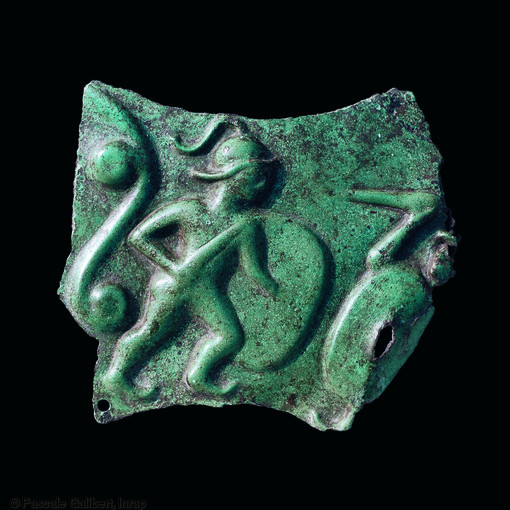 Fragment de tôle de bronze perforée figurant deux guerriers celtes au combat.