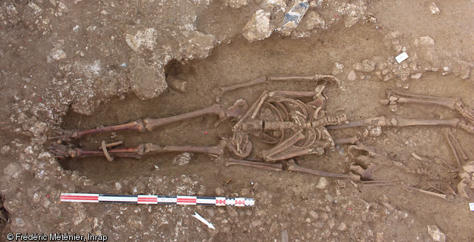 Sépulture 2055 en cours de fouille. Individu masculin inhumé en décubitus, avec présence d'une entrave de fer au membre inférieur gauche, découvert dans une nécropole antique à Saintes (Charente-Maritime).  L'entrave se compose d'un anneau en fer de section circulaire fermé par enroulement. Les deux extrémités du jonc sont définitivement solidarisées par rivetage. Un second anneau a été passé dans l'entrave avant sa fermeture et permet l'enchaînement. Ce mécanisme est donc inamovible et seule une découpe permet de libérer l'individu.